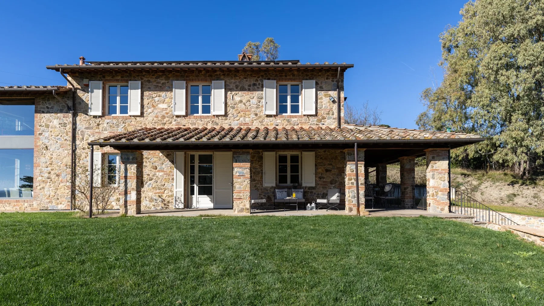 A stone house with a covered patio sits beside a broad green lawn.