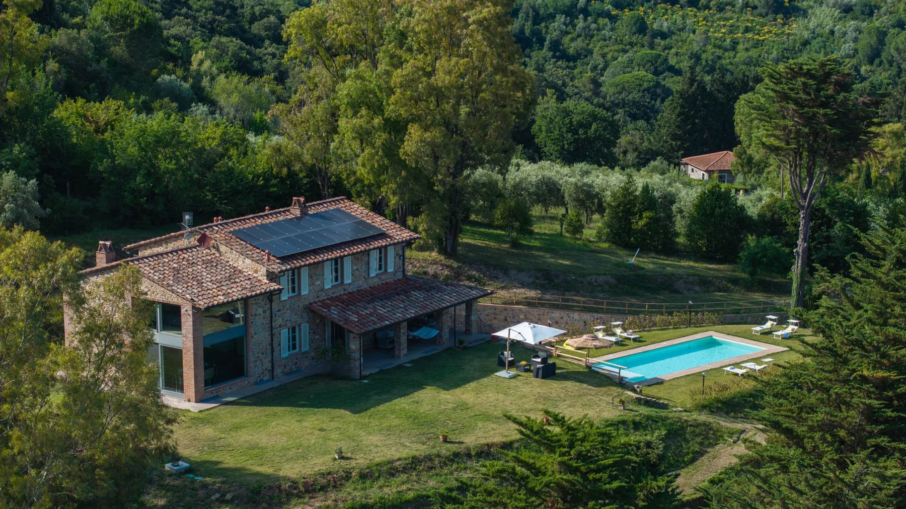 A house and swimming pool sit in a grassy clearing surrounded by trees.