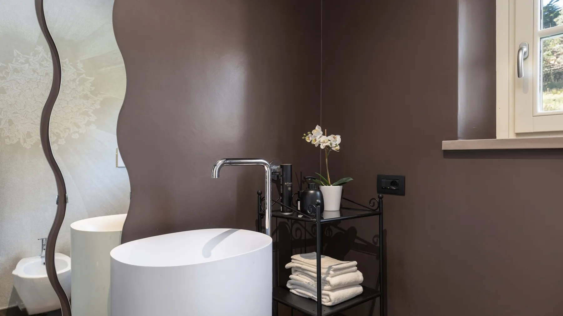 A bathroom with a freestanding bathtub, sink, and towels on a small rack.