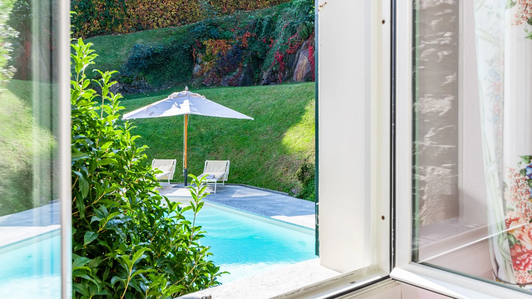 Una piscina y asientos en el patio se ven a través de una ventana abierta.