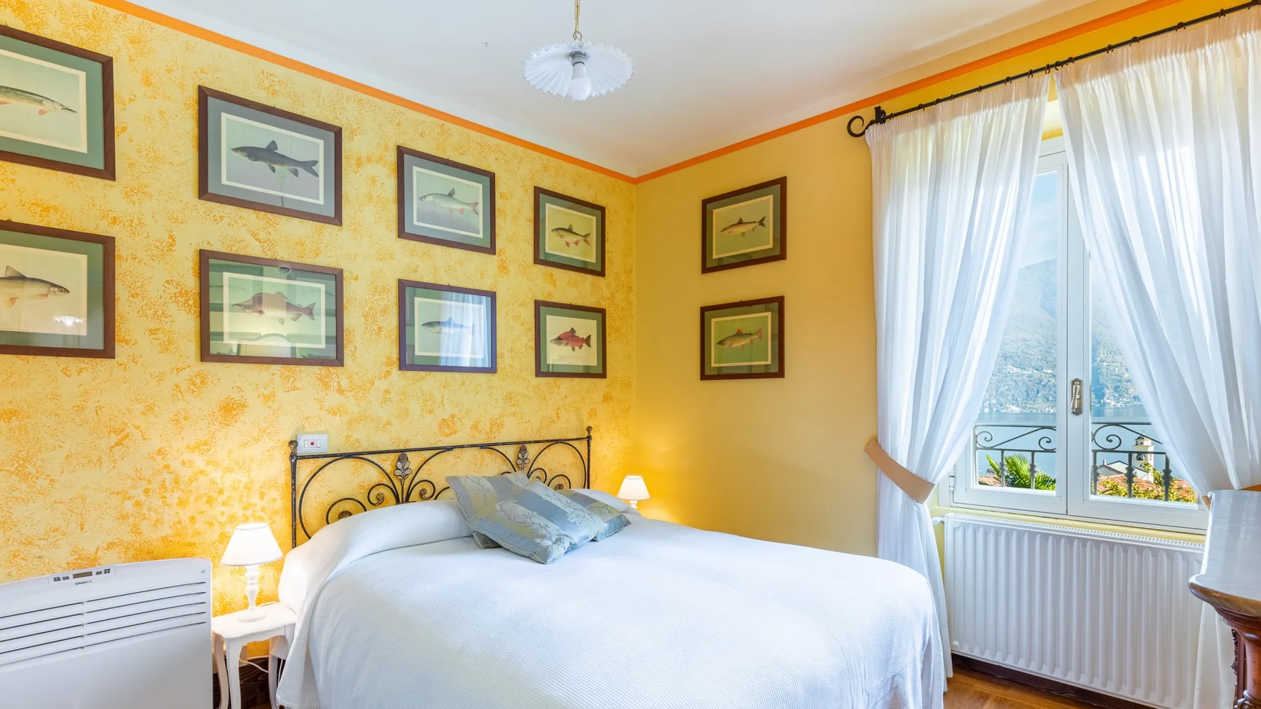 Un dormitorio luminoso con una cama blanca, cuadros enmarcados y una ventana con cortinas.