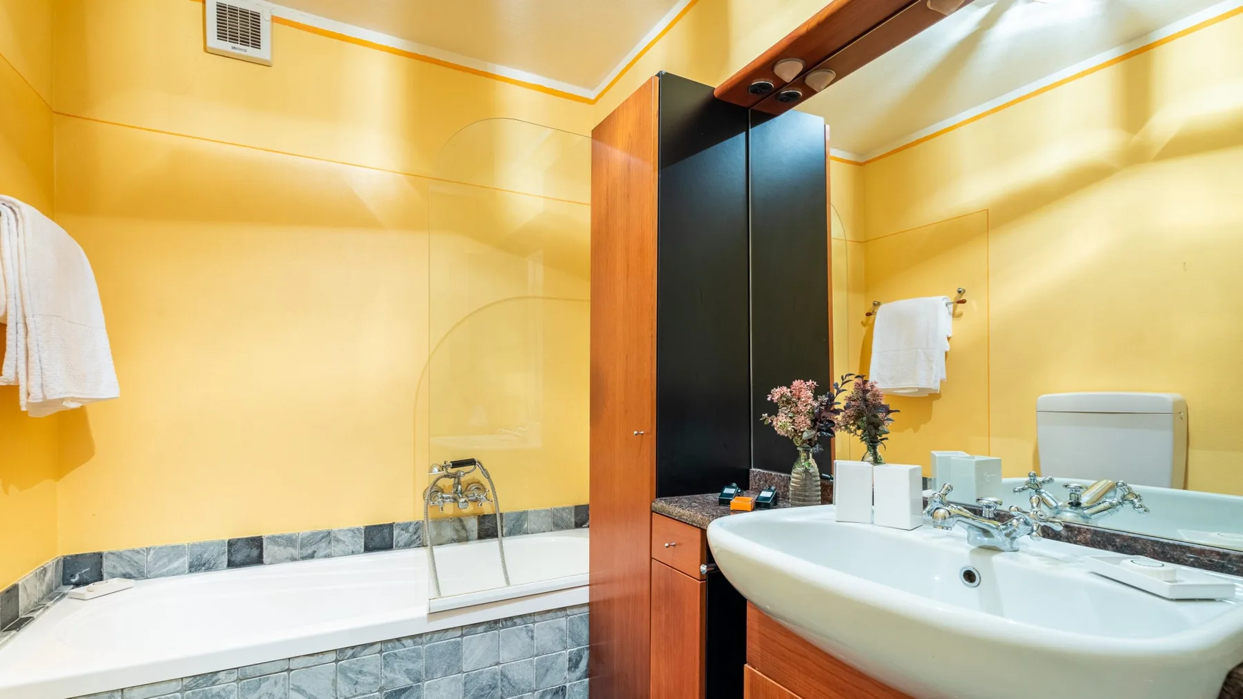Un baño amarillo tiene una bañera, un lavabo y un tocador de madera oscura.