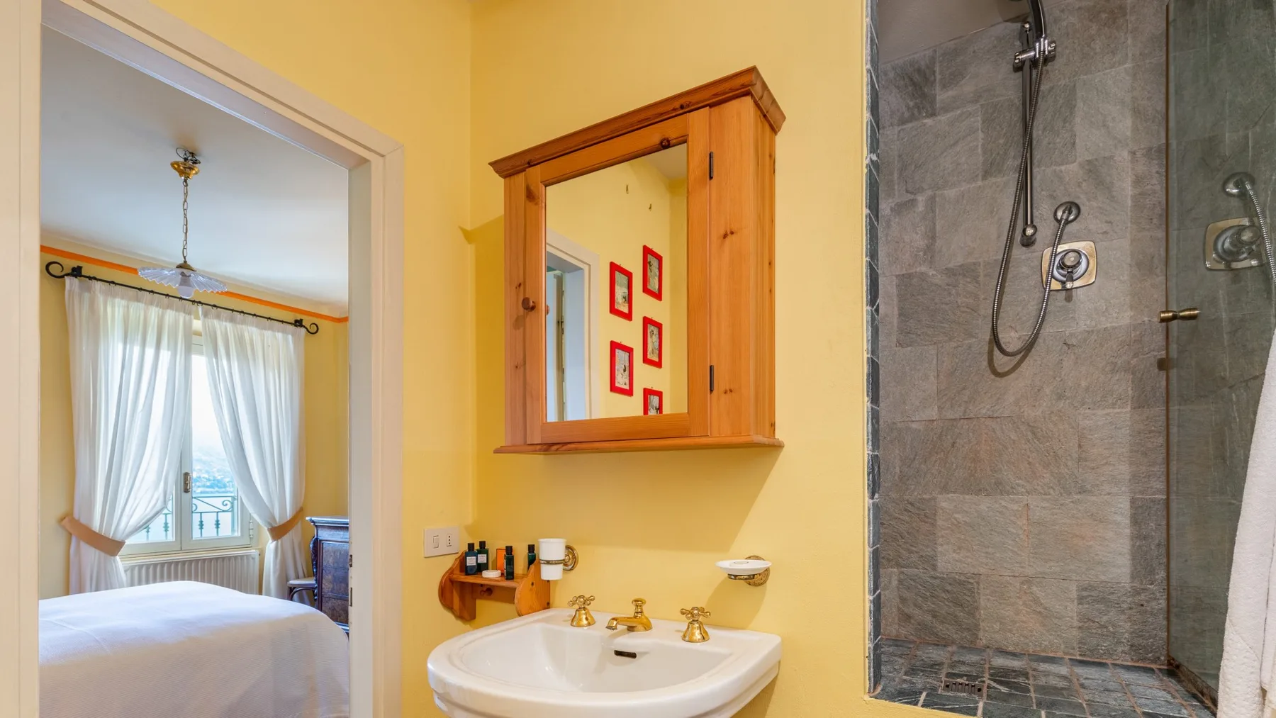 Un baño con lavabo y espejo junto a una puerta abierta hacia un dormitorio.