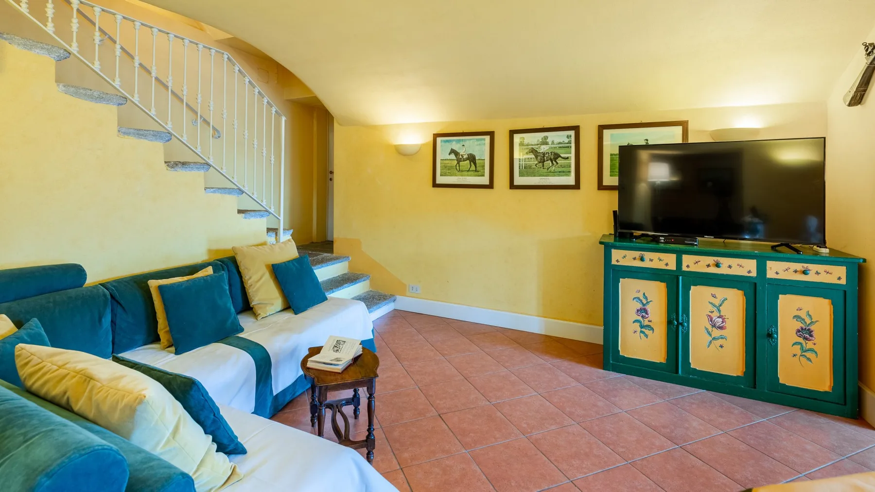 Una sala de estar con asientos bajo una escalera y un televisor sobre un mueble.