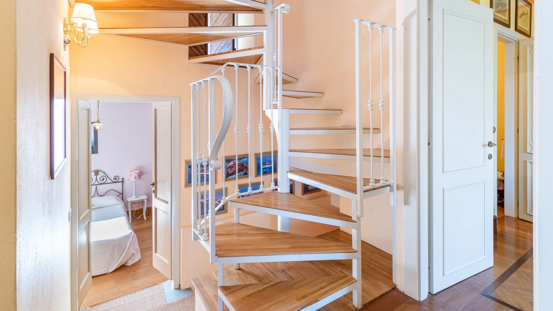 Un pasillo interior luminoso con una escalera de caracol de madera y una puerta abierta.