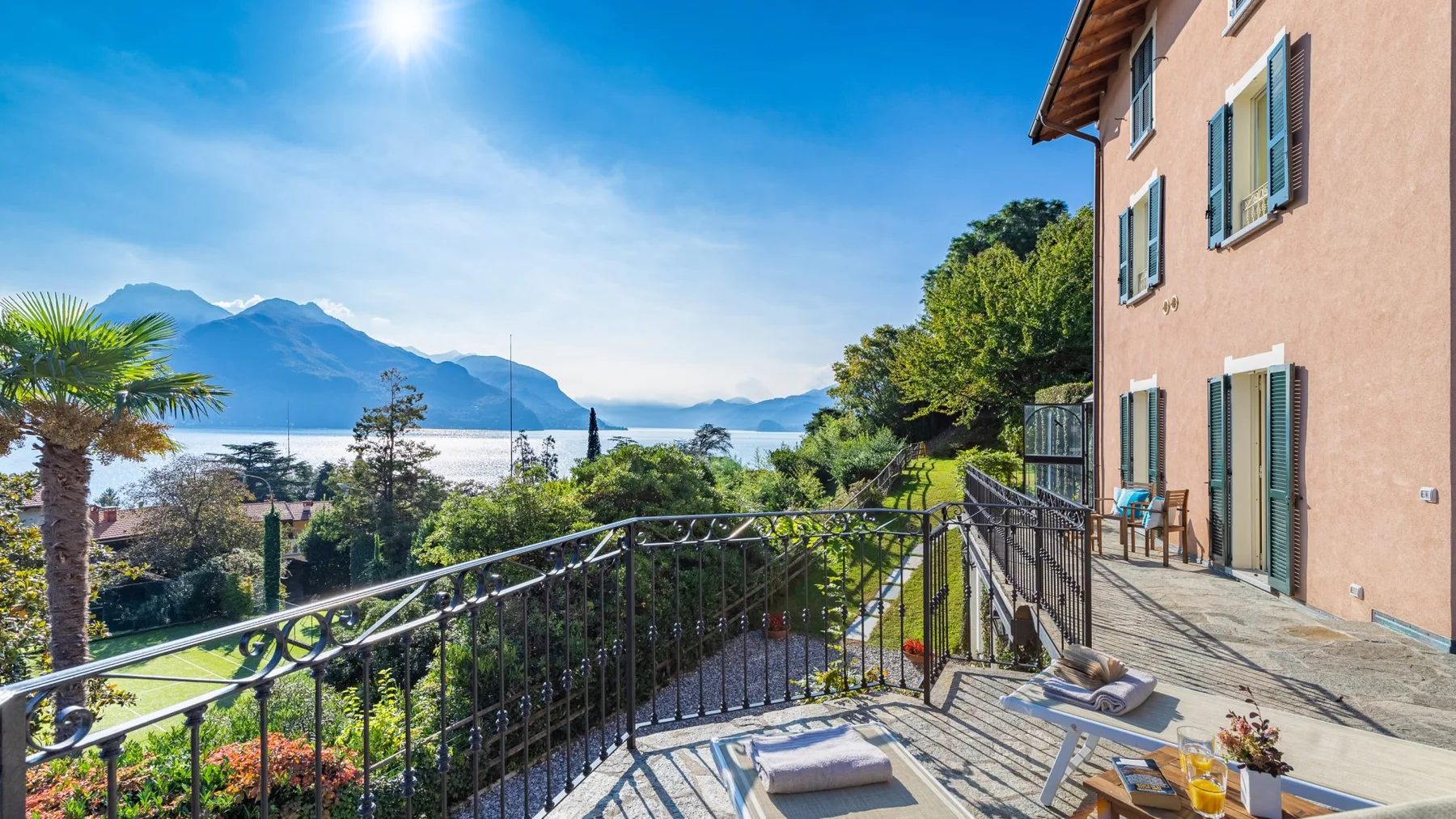 Una terraza exterior soleada tiene vistas a un lago y montañas lejanas.