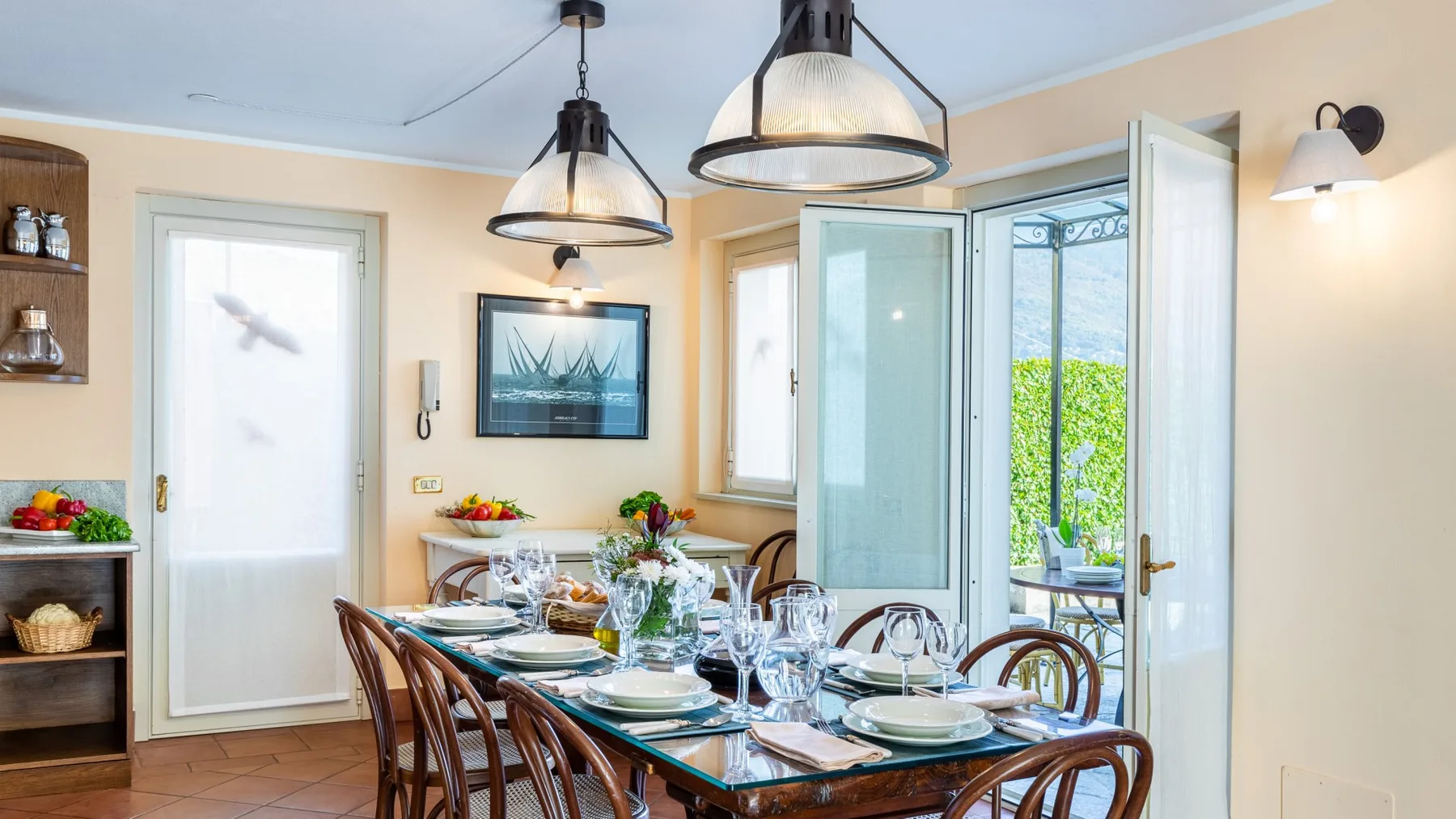 Un comedor con la mesa puesta junto a puertas abiertas al jardín.