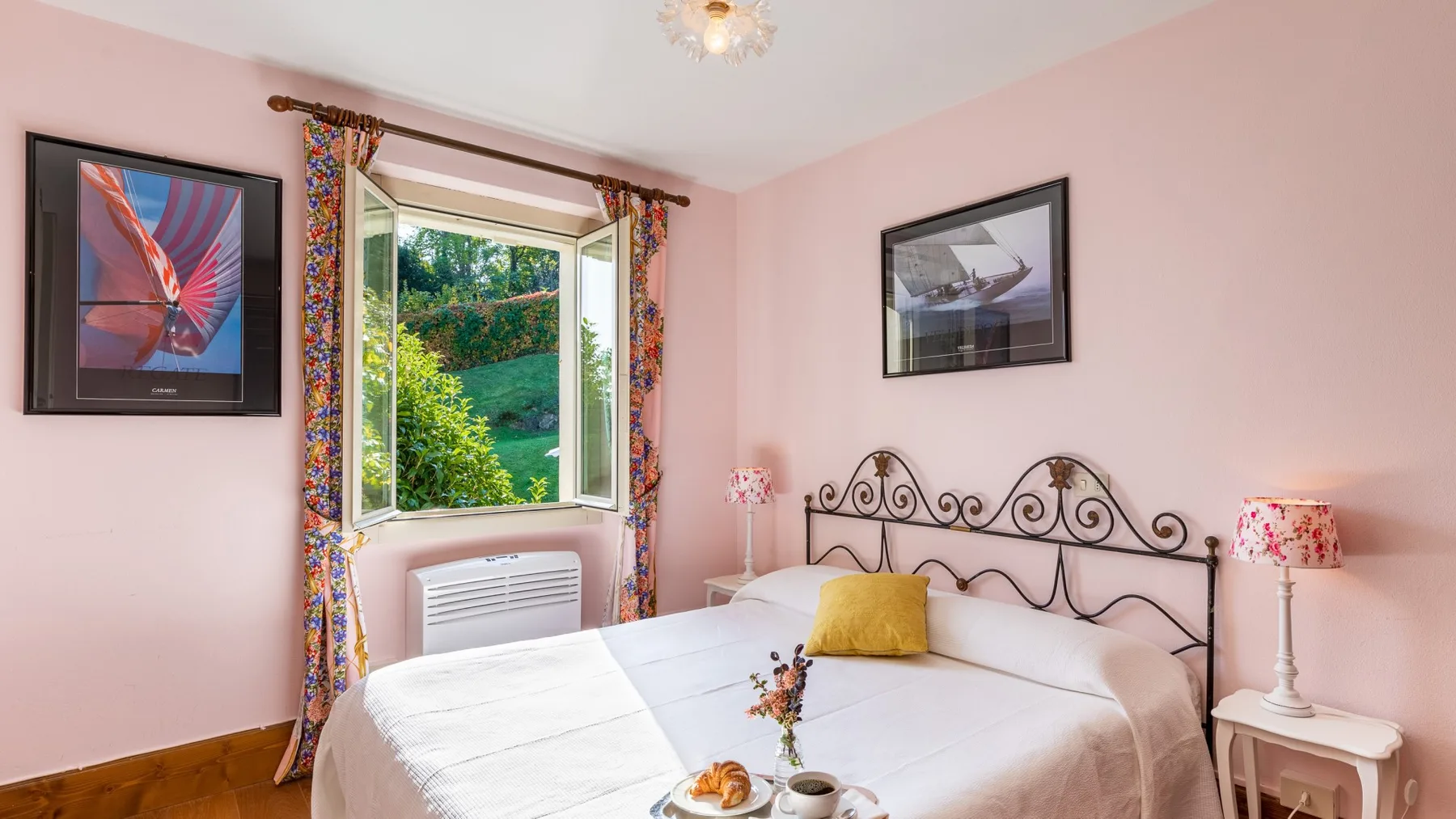 Un dormitorio con una cama, un cabecero de metal decorativo y una ventana con vistas a la vegetación.