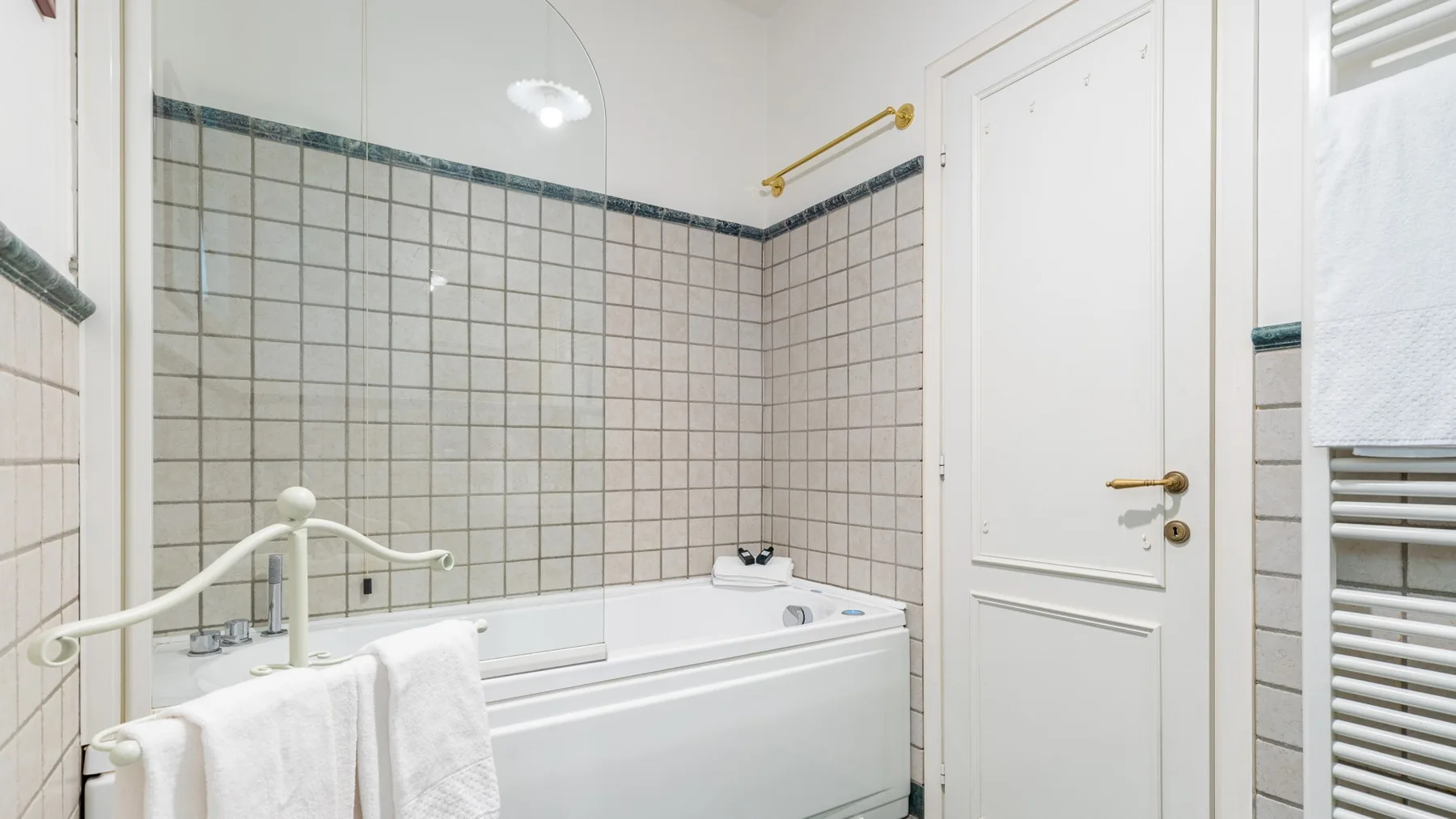 Un baño revestido de azulejos con bañera y una puerta blanca.