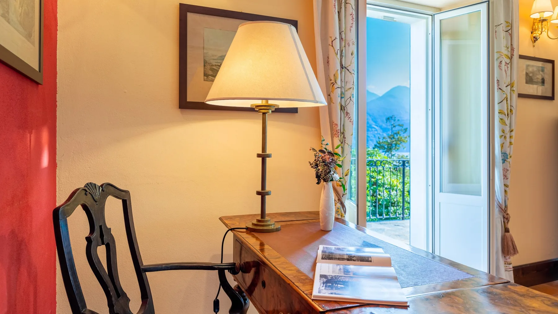 Una habitación cálidamente iluminada con un escritorio junto a una puerta abierta al balcón.