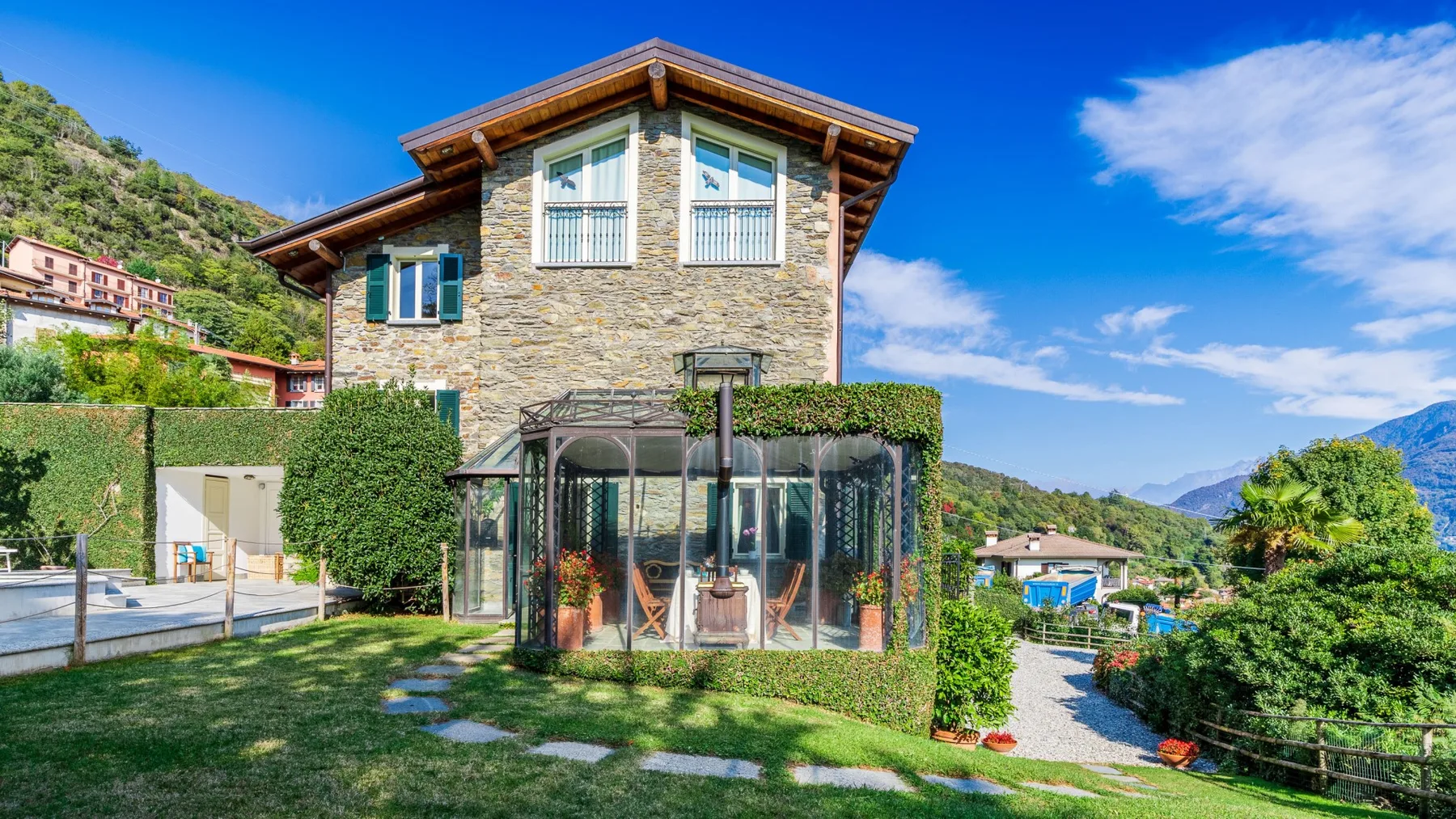 Una casa de piedra se encuentra junto a un patio acristalado y un jardín.