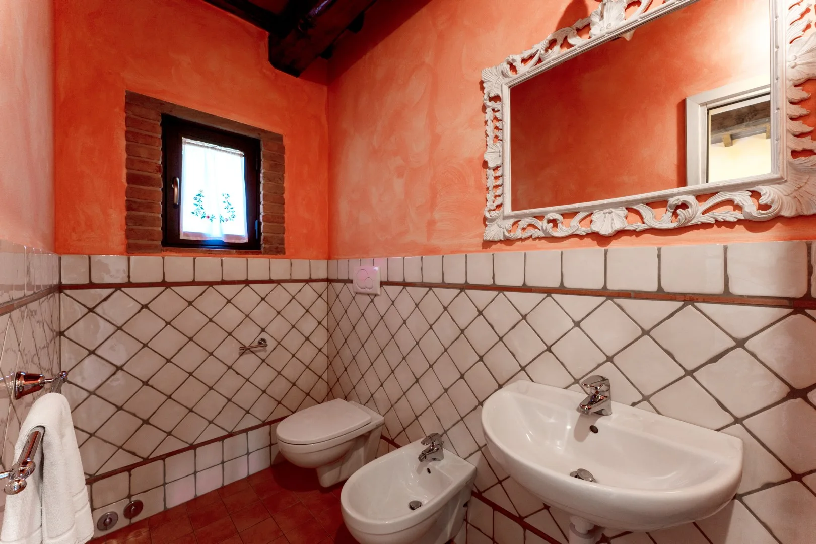Un baño con paredes color terracota, azulejos en la parte inferior y lavabo, inodoro y bidé.