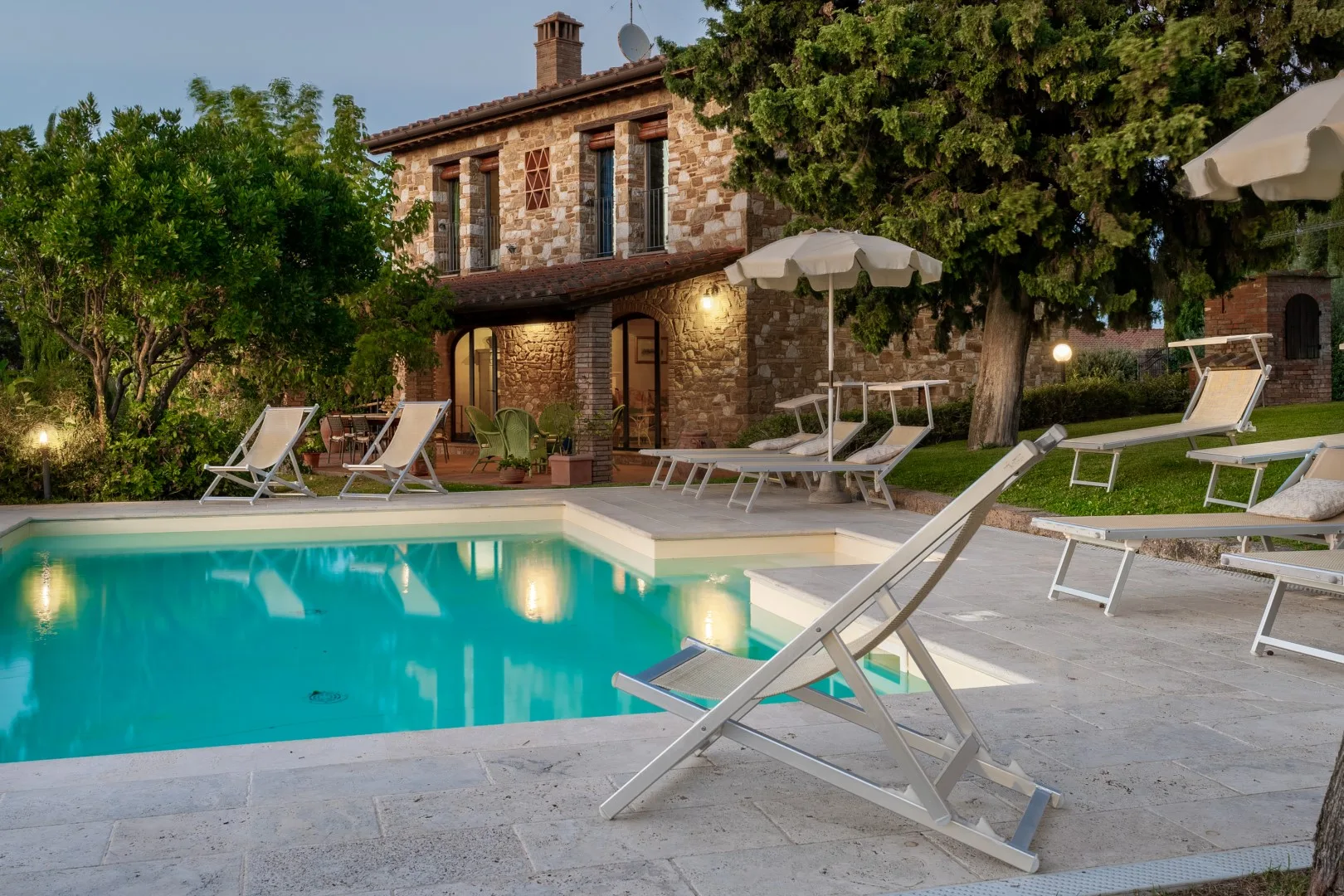 Una piscina con tumbonas y sombrillas está junto a una casa de piedra de dos plantas.