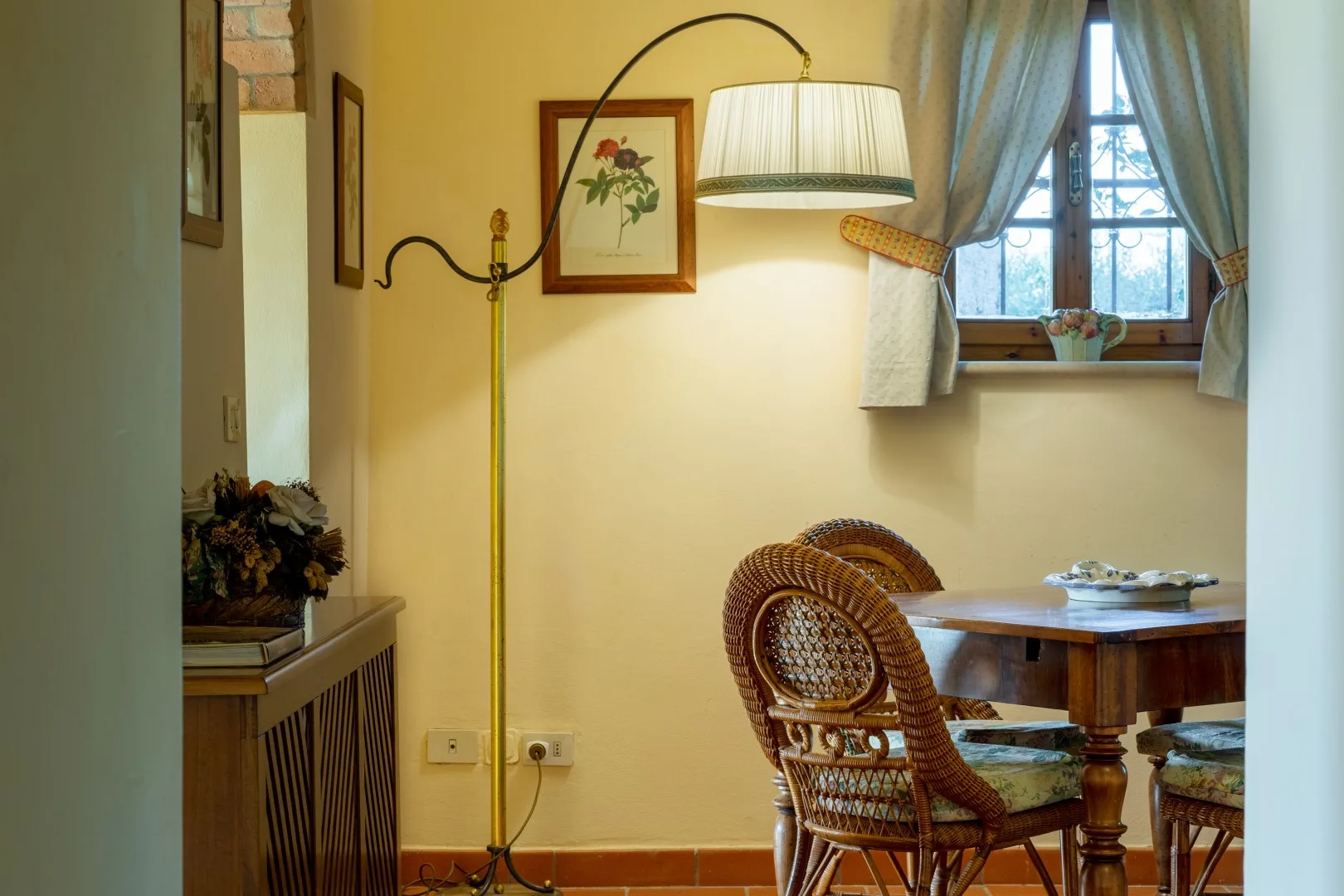 Un rincón comedor iluminado tiene una mesa de madera, sillas de mimbre y una ventana con cortinas.