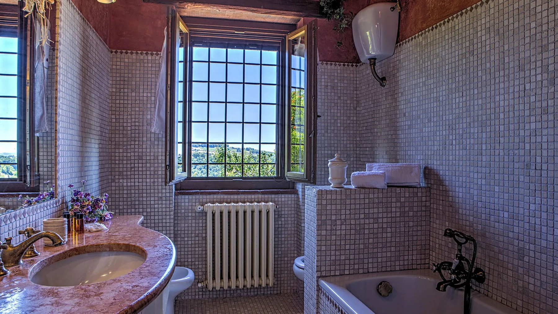 A tiled bathroom has a curved sink, bathtub, radiator, and large grid-paned windows.