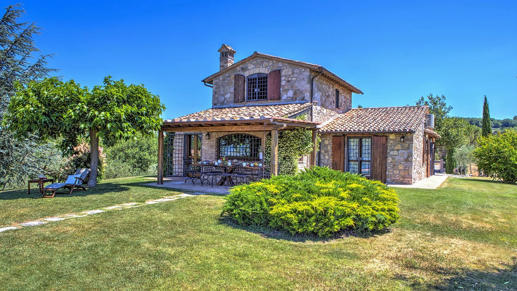 A stone country house with a tiled roof, covered patio, and landscaped lawn.