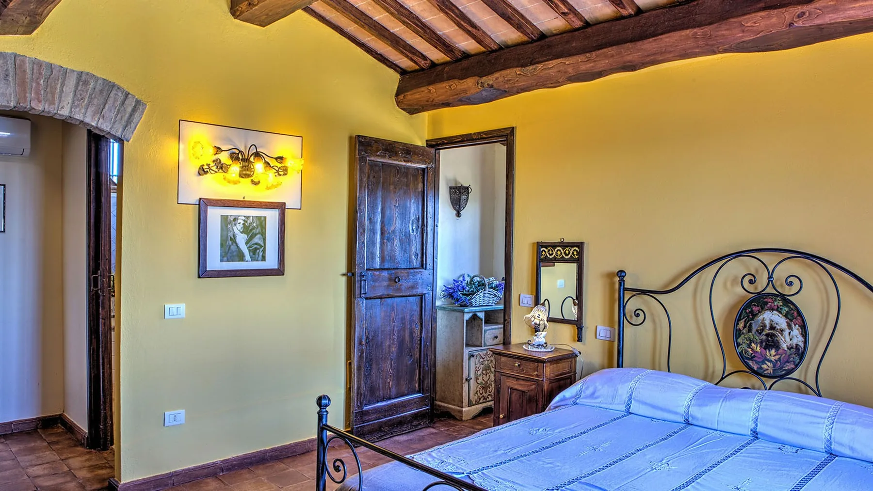 A bedroom with a black wrought-iron bed, blue bedding, dark wood doors, and exposed ceiling beams.
