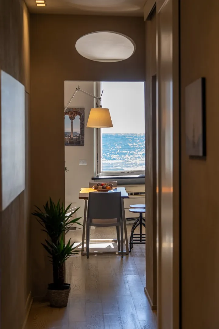 A narrow hallway opens onto a dining nook with a table, pendant lamp, and ocean view.