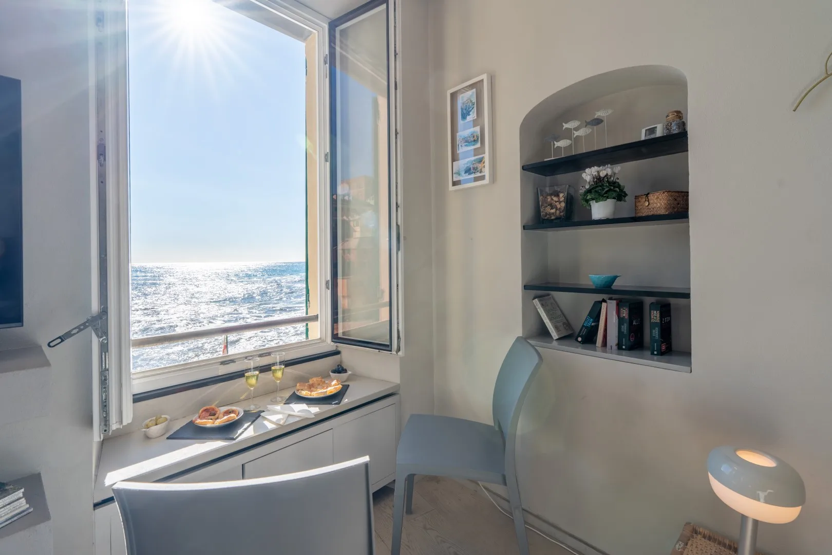 A bright sitting area overlooks the sea through an open window, with a built-in shelf and small table.