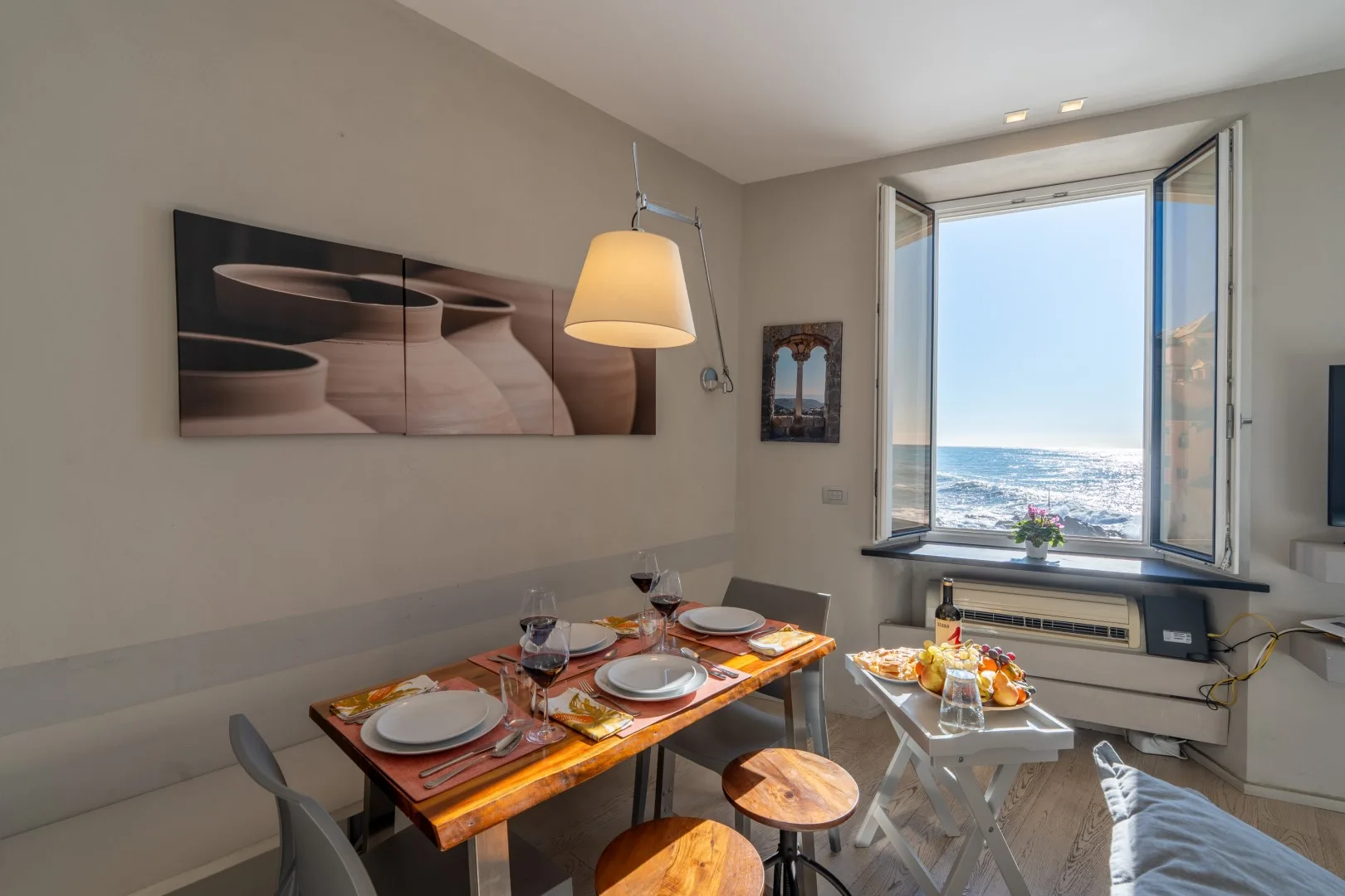 A dining area has a set table beside an open window overlooking the sea.