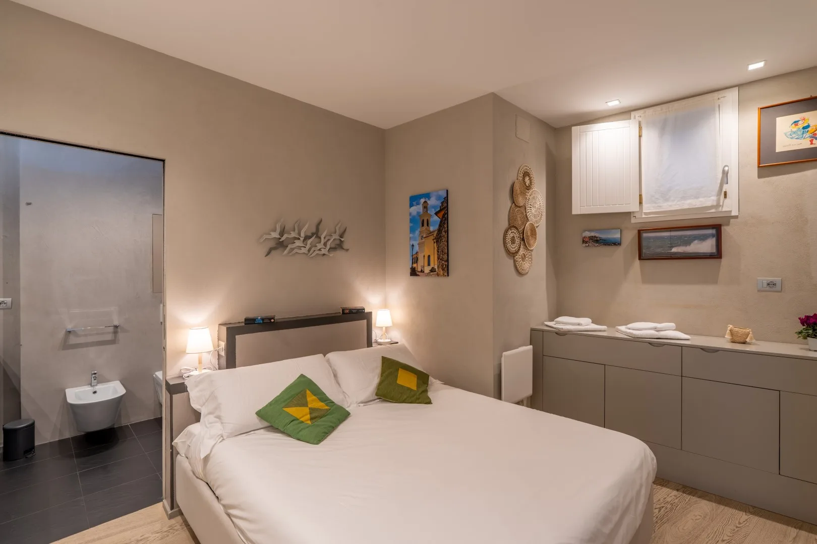 Bedroom with a neatly made double bed, green accent pillows, and built-in cabinets along the wall.