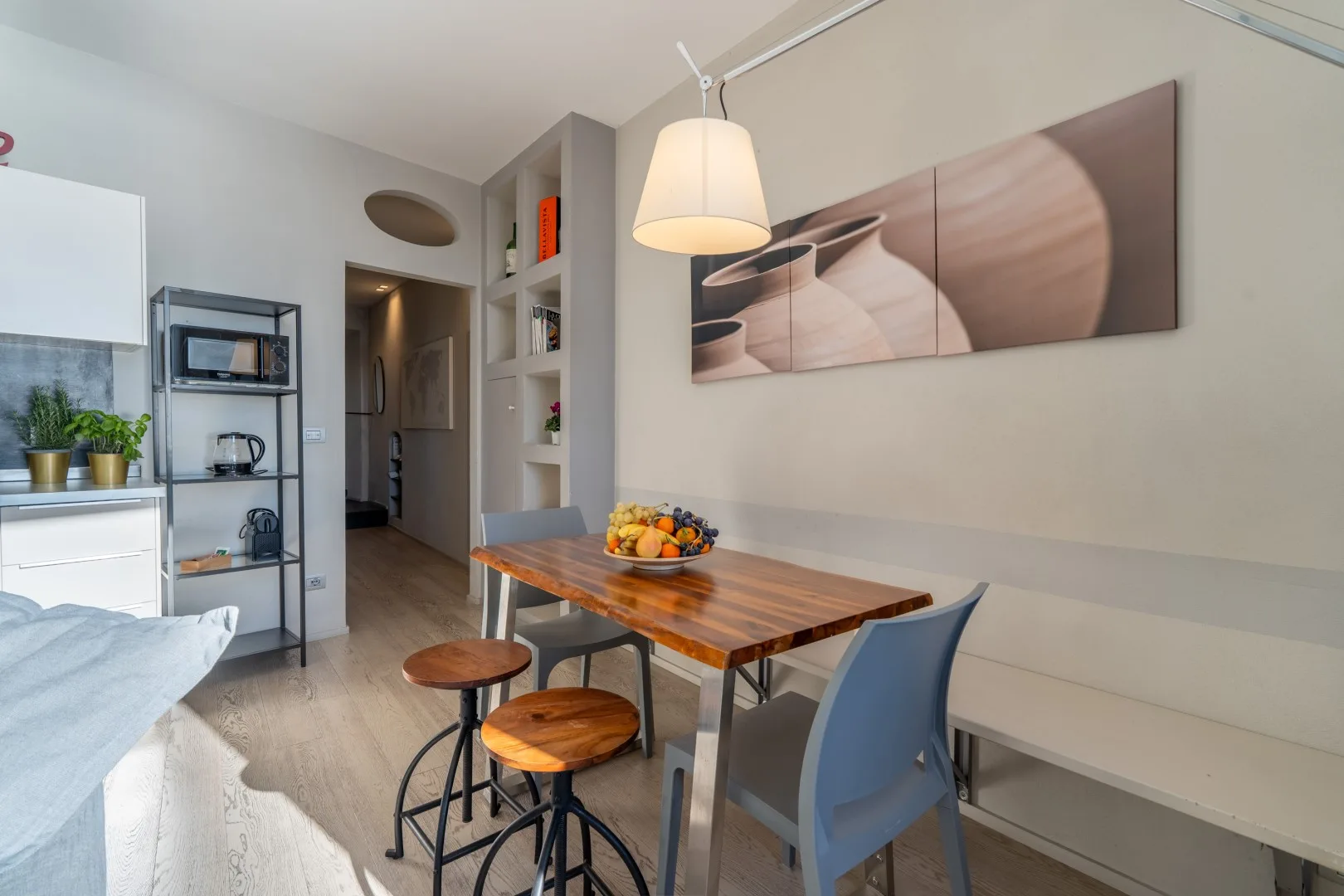 A dining area has a wooden table, stools, a blue chair, and abstract wall art.