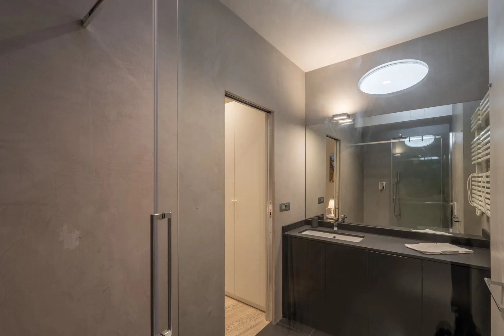 A modern bathroom has a wide vanity, a large mirror, a glass shower, and a heated towel rail.