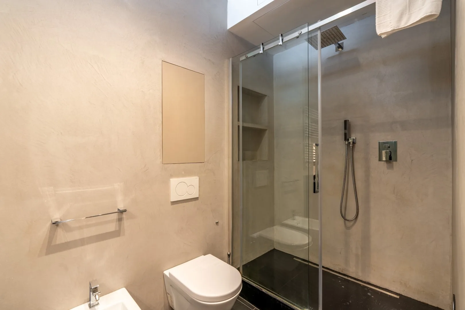 A modern bathroom with a glass shower enclosure, wall-mounted shower, toilet, and sink.