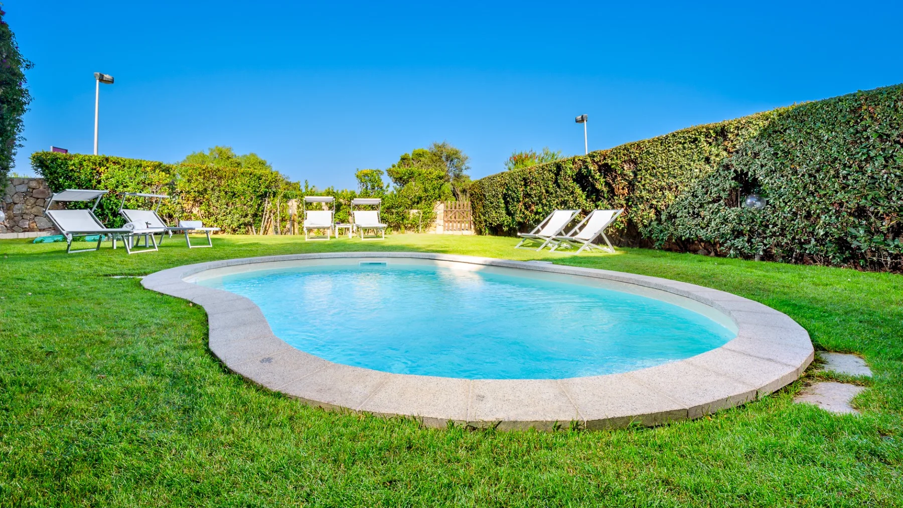 Una piscina al aire libre está rodeada de césped y setos de jardín.