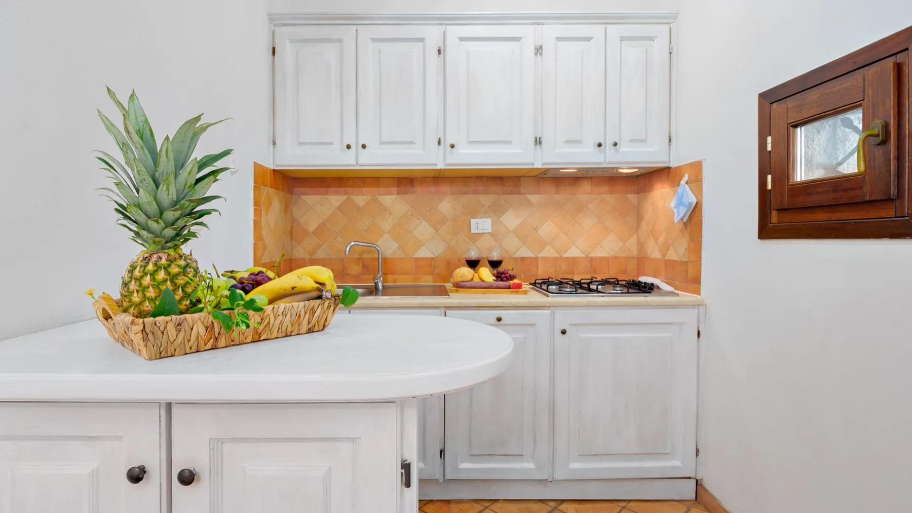 Una cocina luminosa con gabinetes blancos, una encimera y fruta sobre la isla.
