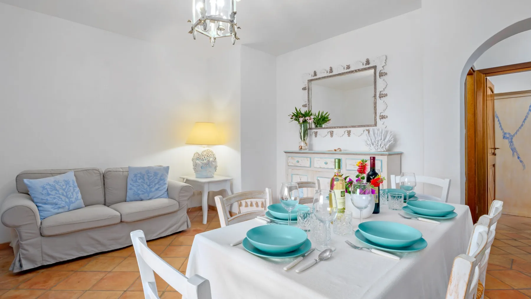 Un comedor con una mesa preparada con vajilla turquesa bajo una lámpara de araña.