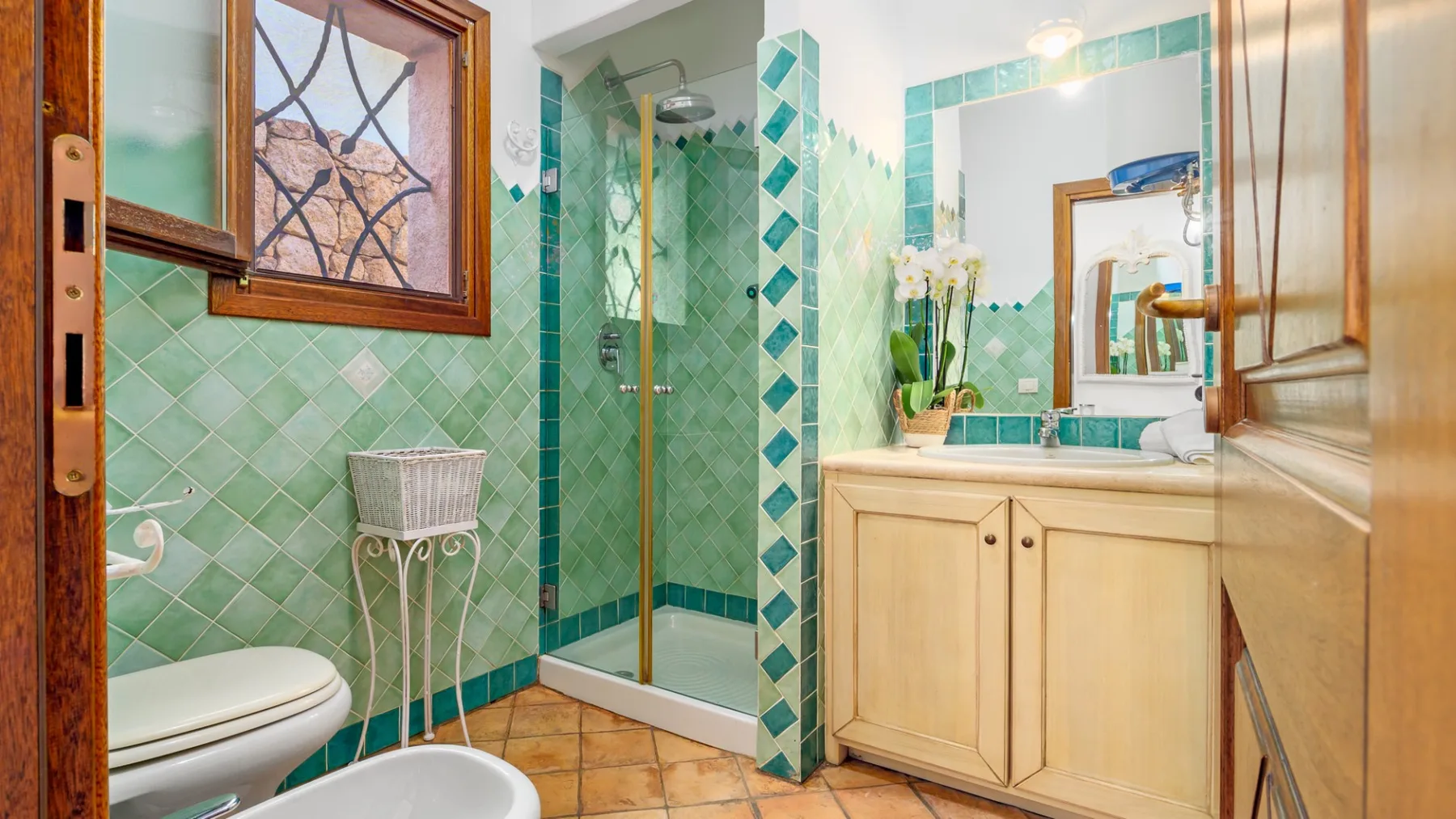 Un baño alicatado con ducha de vidrio, lavabo con mueble e inodoro.