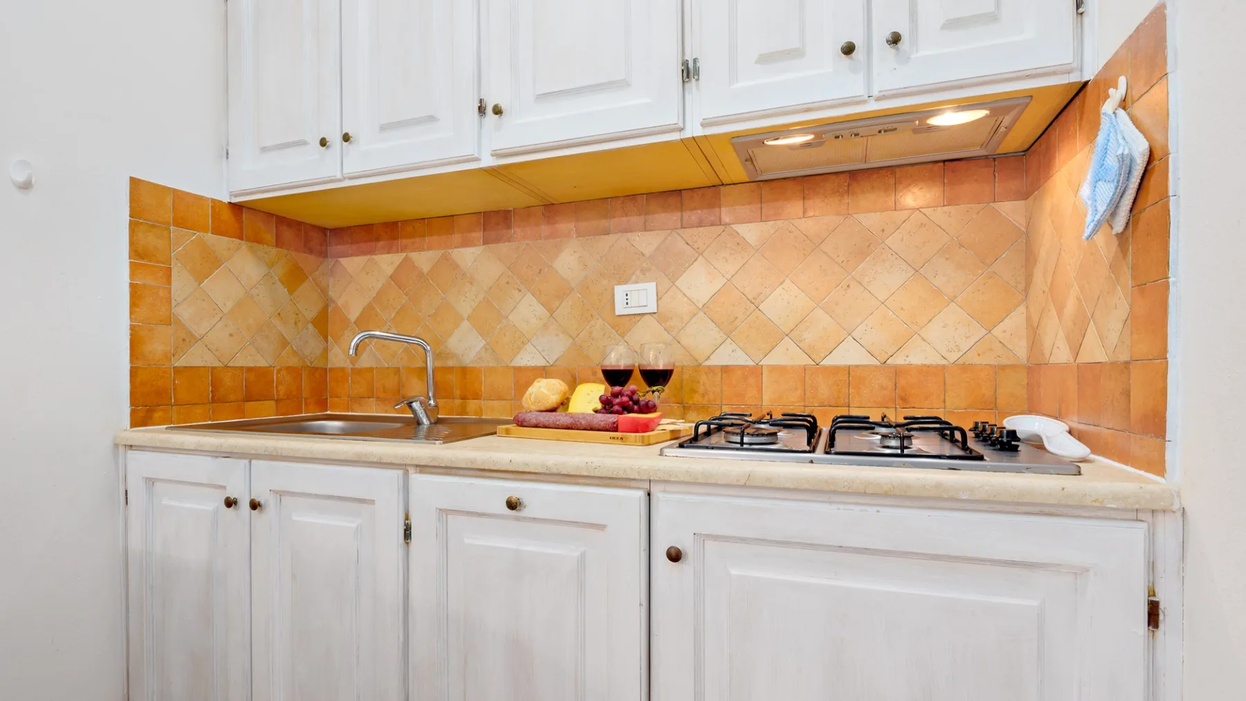 Una cocina compacta con gabinetes blancos, fregadero y estufa de gas.