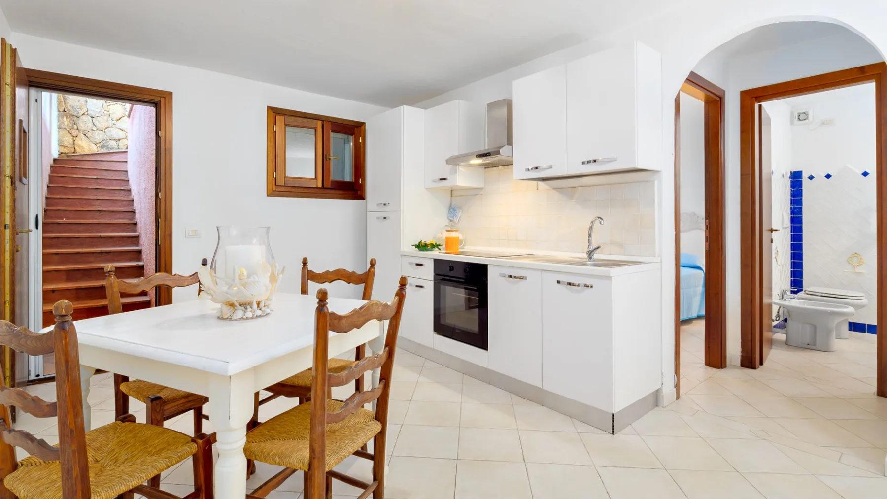 Comedor junto a una cocina compacta, con una escalera visible a través de la puerta.