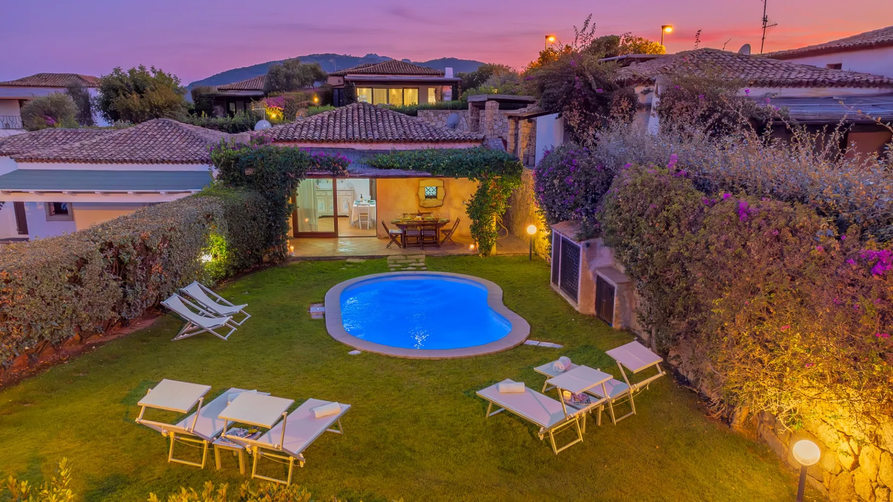 Un jardín ajardinado con piscina y asientos al aire libre al anochecer.