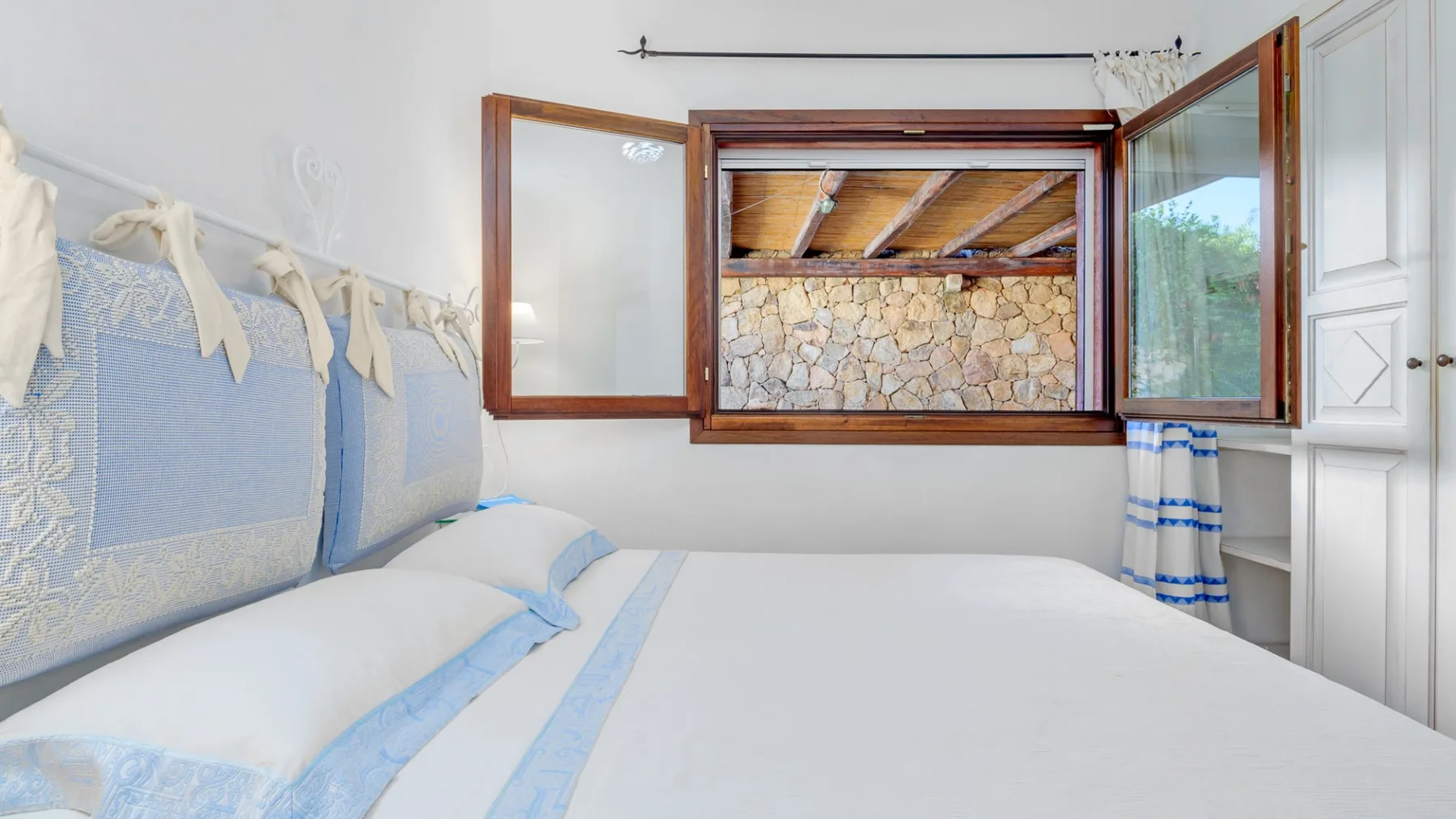 Un dormitorio luminoso con una cama bien tendida y ventanas abiertas.