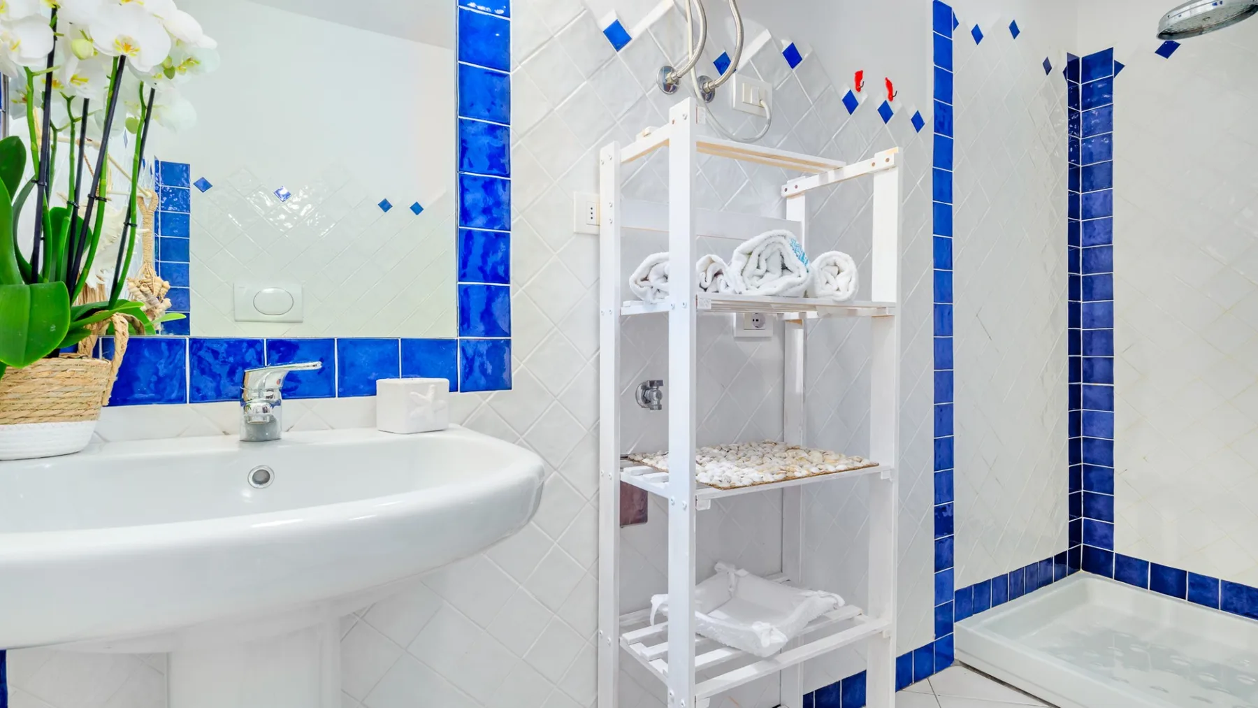 Un baño alicatado con lavabo, toallas en una estantería y ducha.