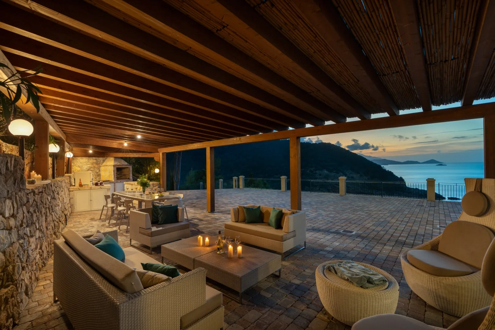 A covered outdoor lounge opens onto a paved terrace overlooking the sea.