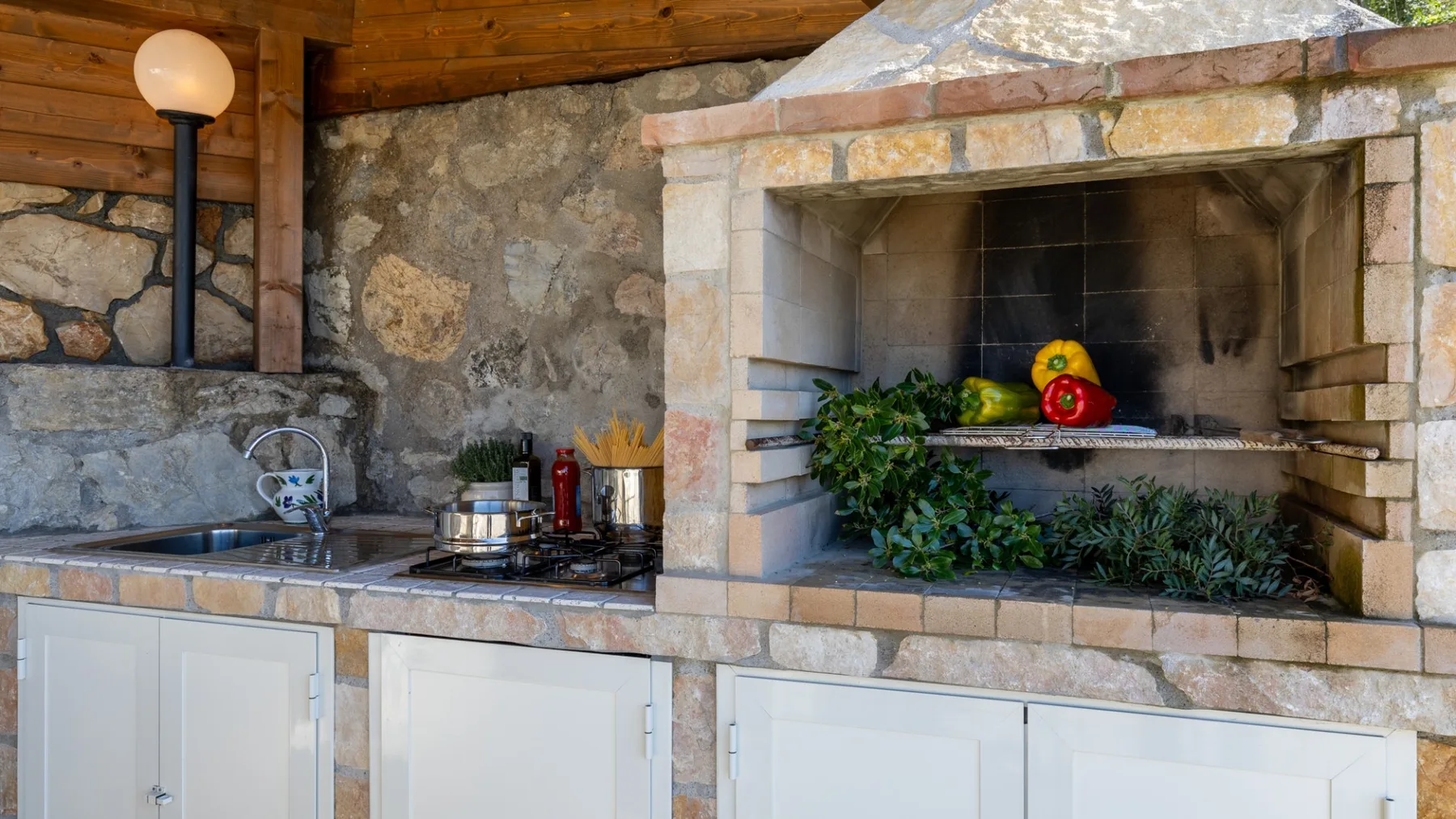 A rustic kitchen with a stone fireplace and a counter holding a sink and cooktop.