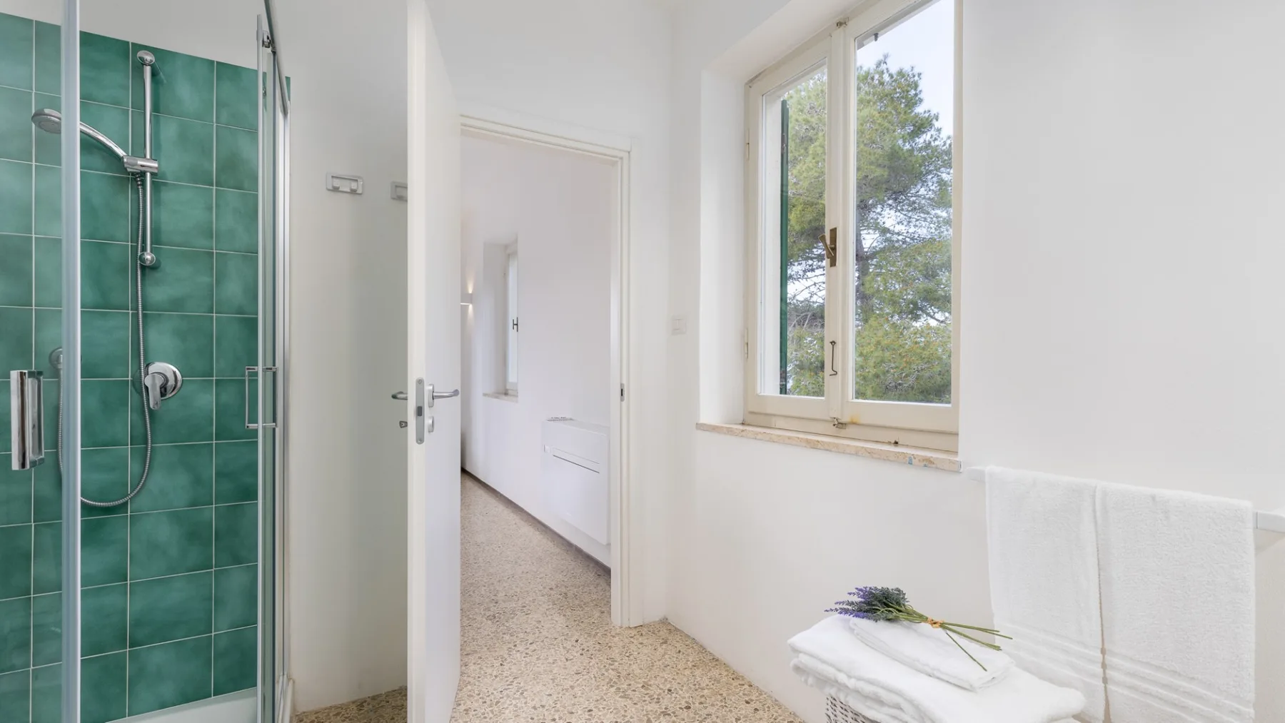 A bright bathroom with a glass shower and a window overlooking trees.