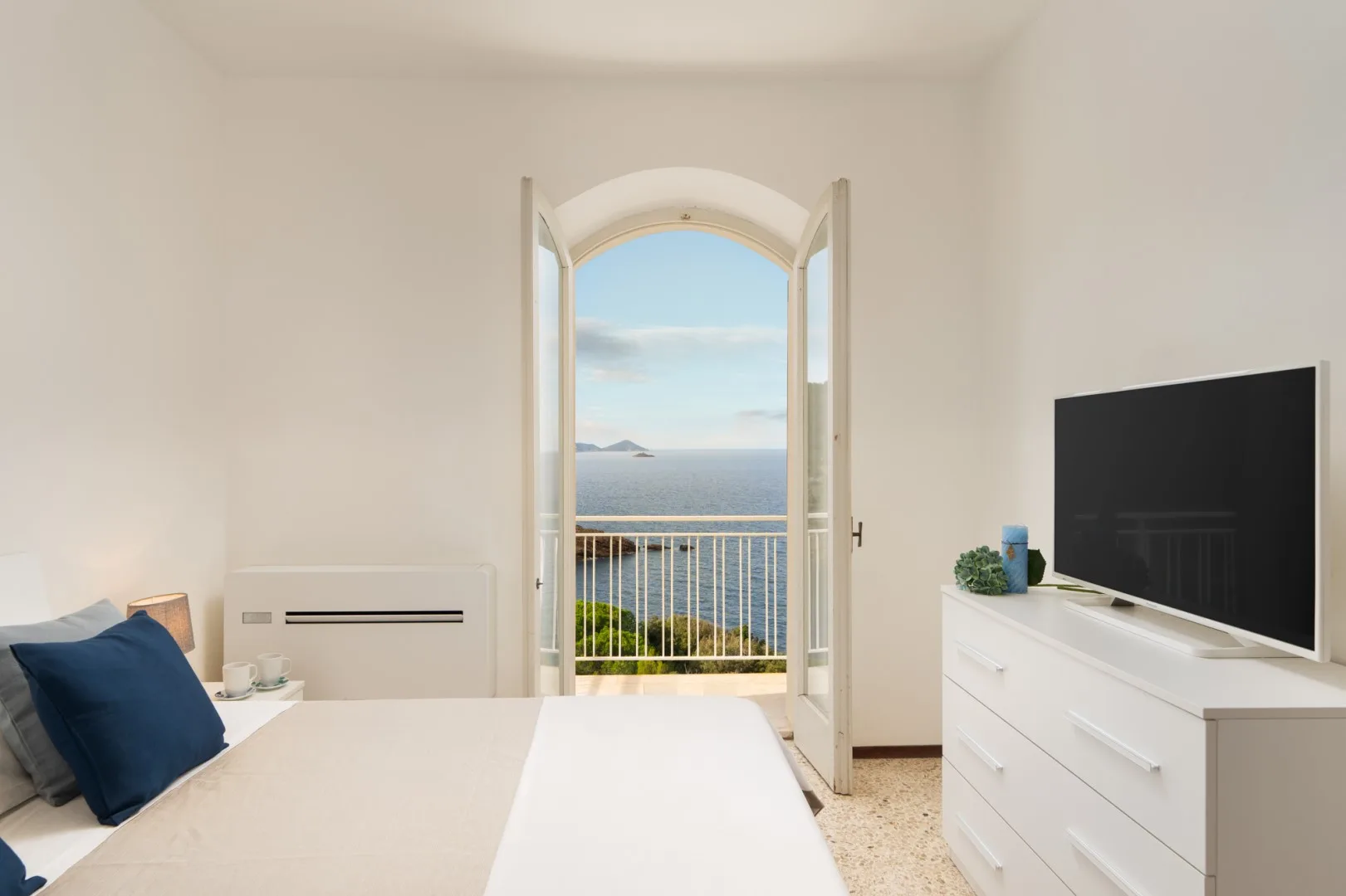 A bright bedroom opens onto a balcony with a sea view.
