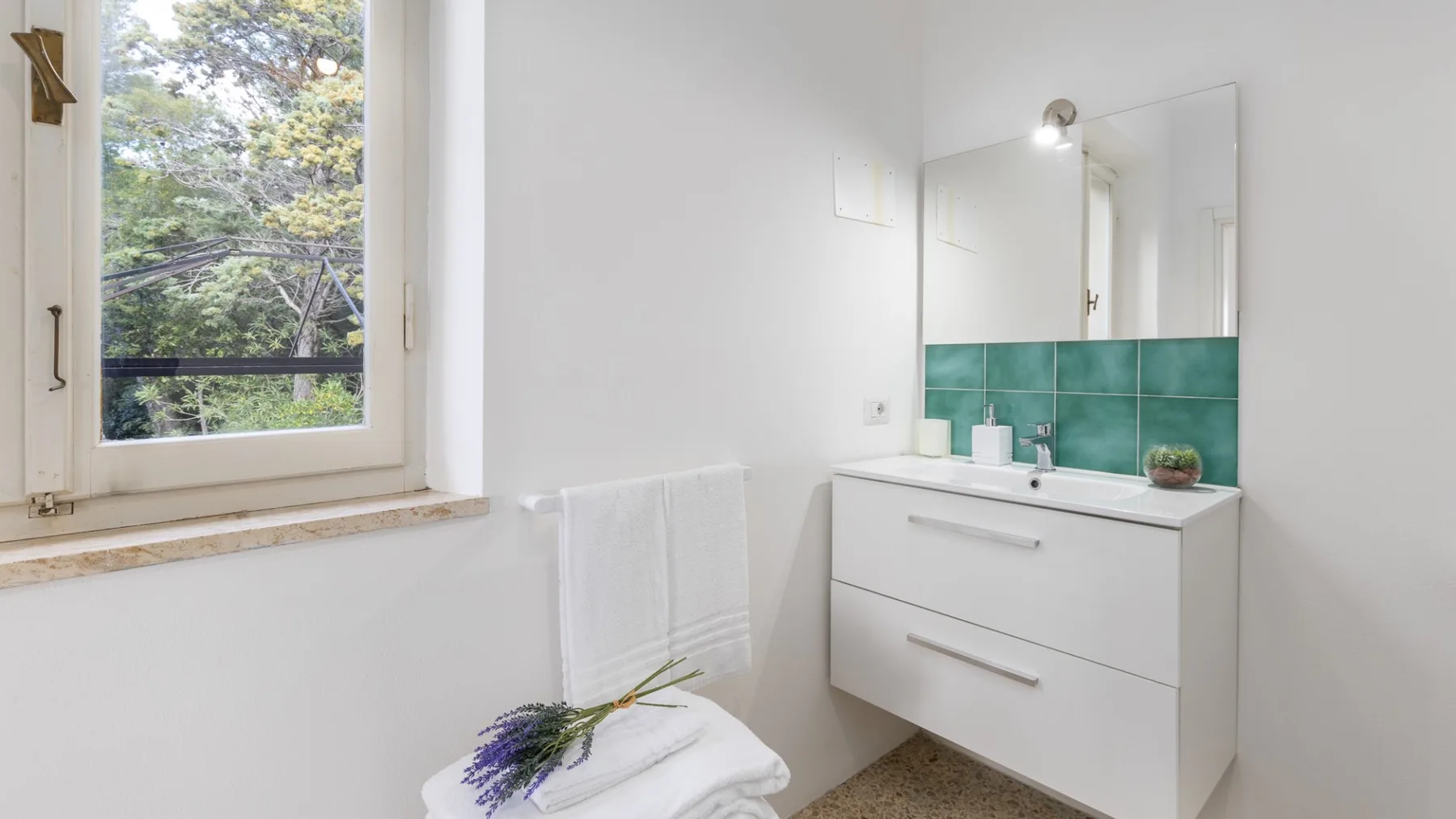 A bright bathroom with a window, mirror, and white vanity.