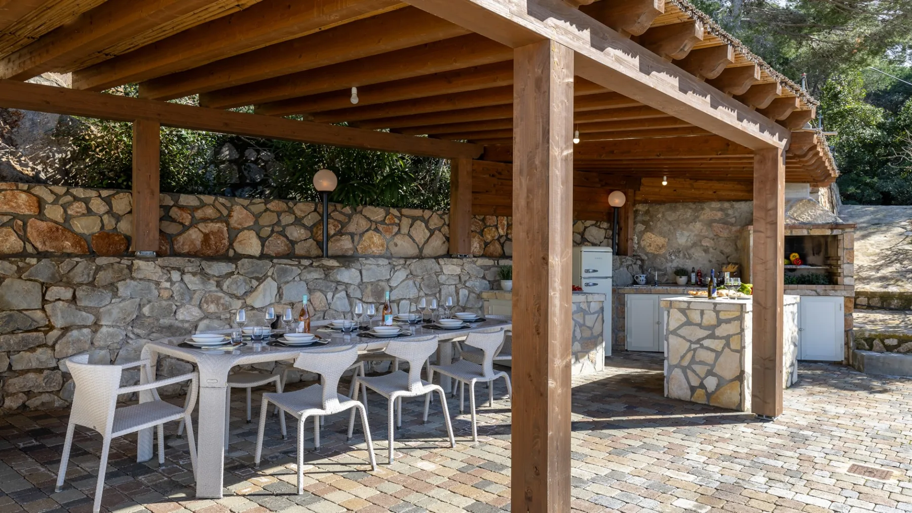A covered outdoor dining area with a long table and an outdoor kitchen.