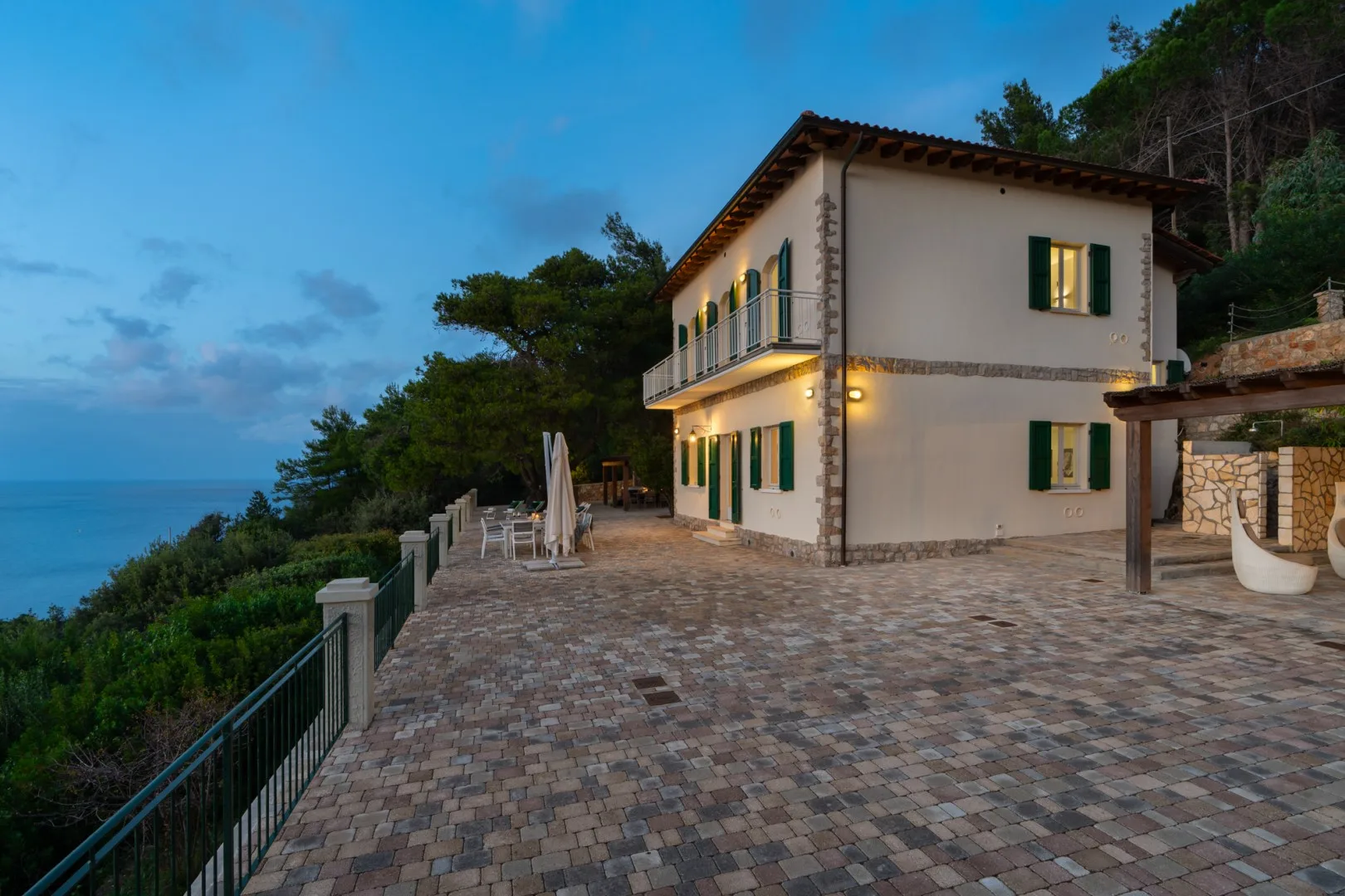 A two-story house opens onto a broad paved terrace overlooking the sea.