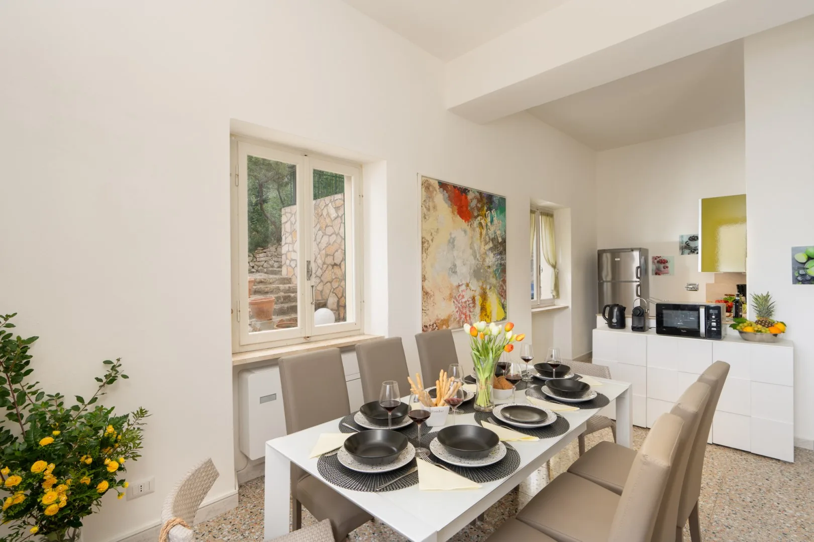A dining area with a set table, beige seating, and colorful wall art.