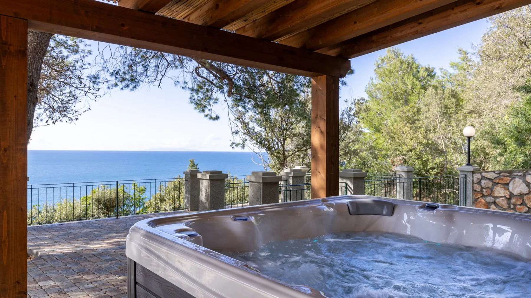 A covered outdoor hot tub overlooks the ocean beside a stone-paved terrace.