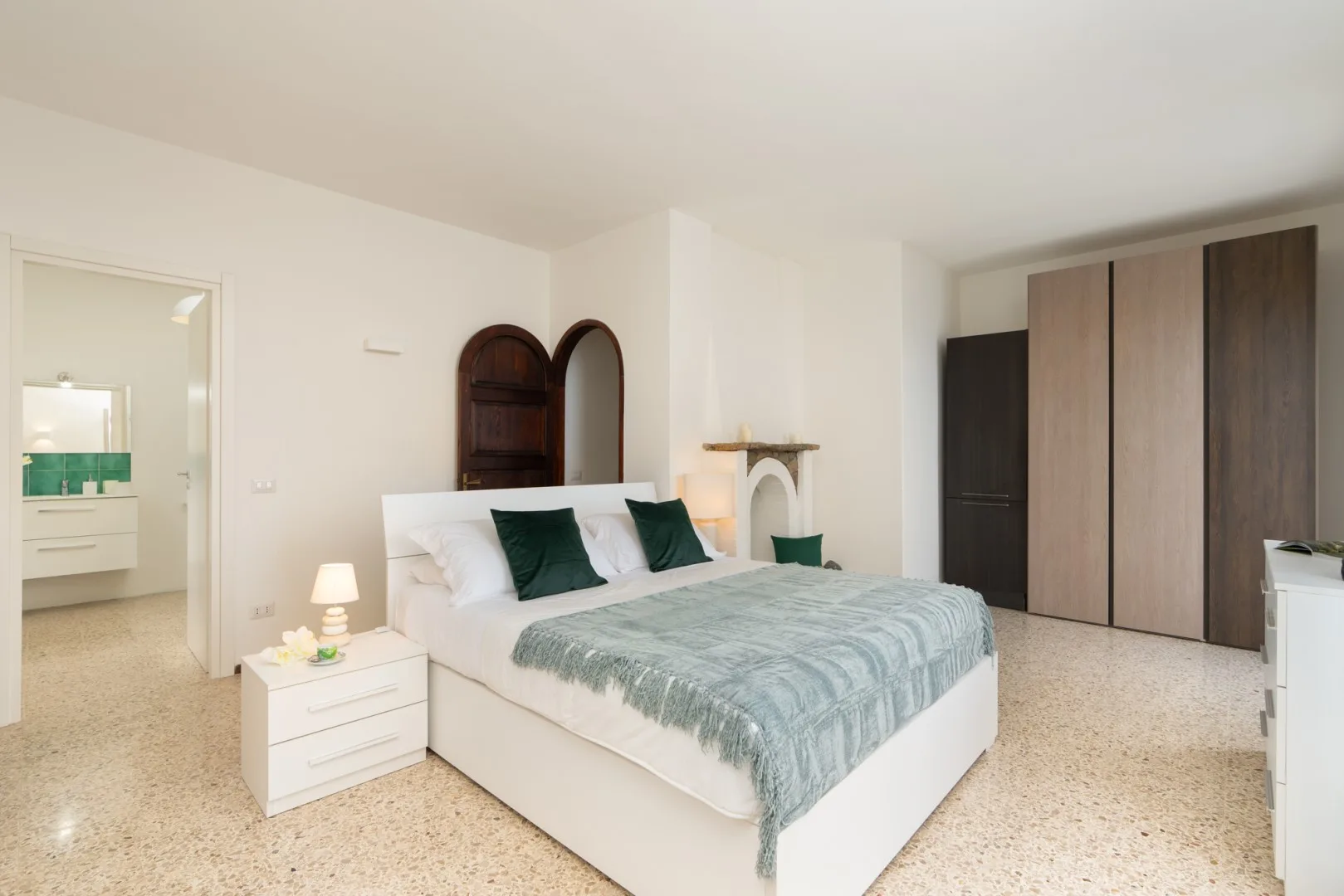 A bedroom with a white bed, pale blue-green bedding, and a large wardrobe.