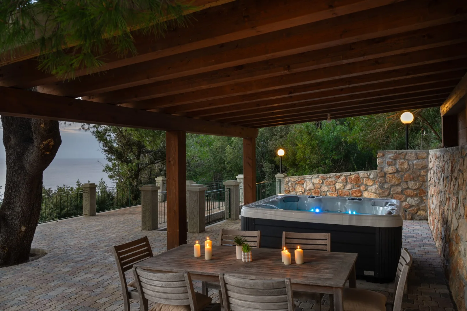 A covered outdoor patio has a dining table beside a lit hot tub.