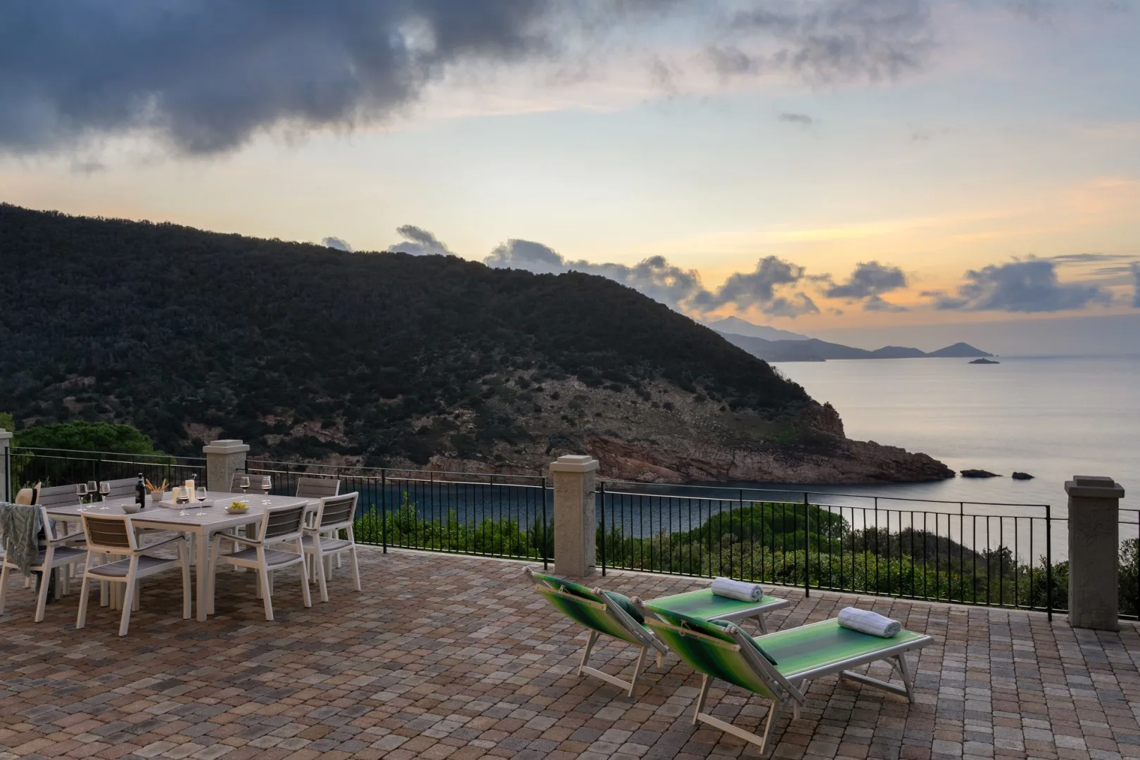 A tiled patio overlooks the sea at sunset, with outdoor seating.