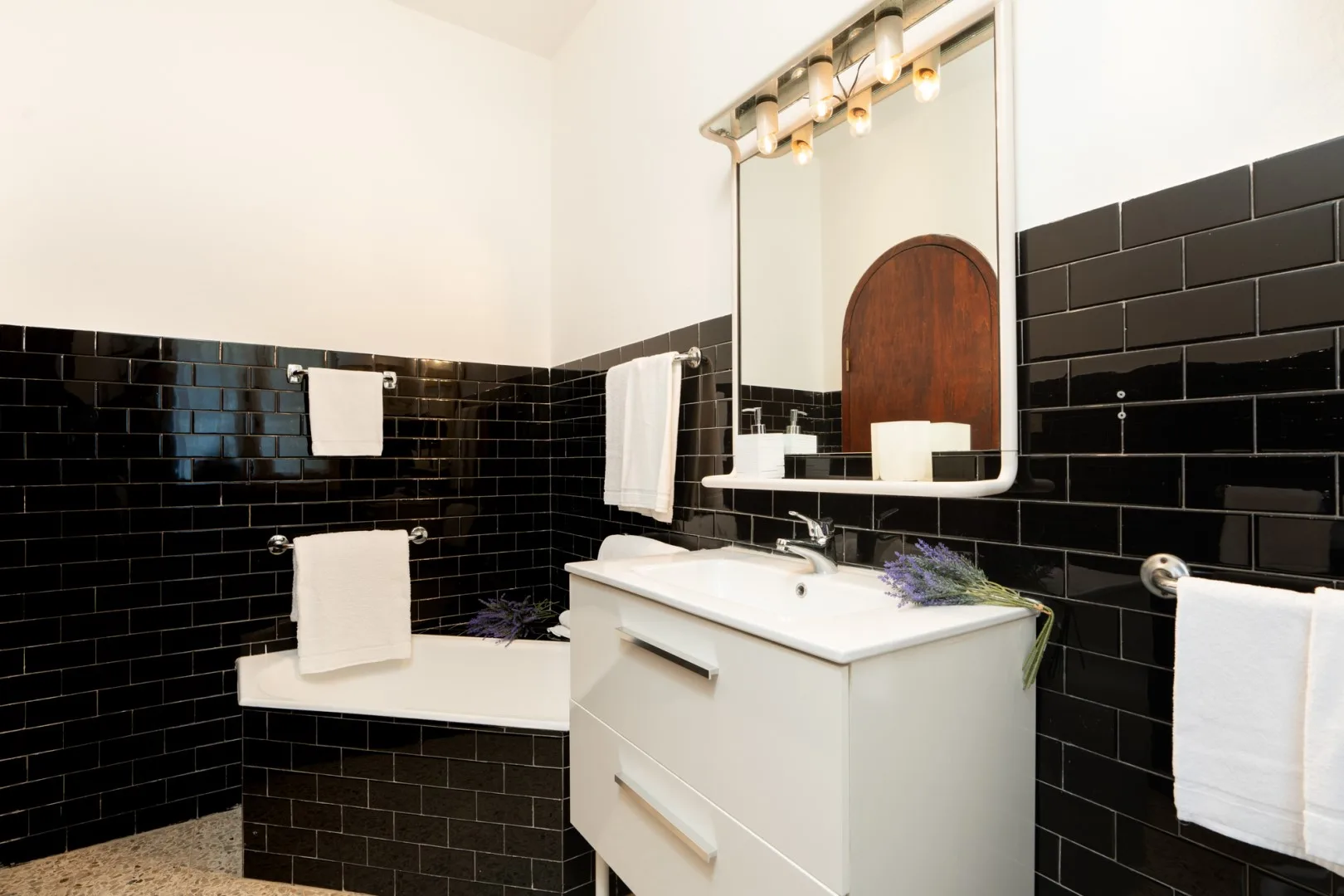 A bathroom with a white vanity, mirror, and black tiled walls.